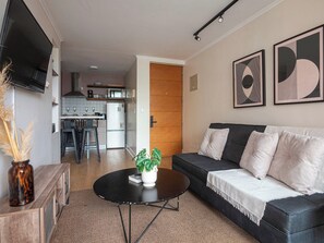 Ein modernes Wohnzimmer mit einer schwarzen Couch, einem Couchtisch und einer Küche im Hintergrund.