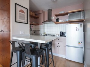 A kitchen with a white countertop, bar stools, a stainless steel refrigerator, and a microwave above the counter. - Costa Home - Escuela Militar & WIFI & Moderno (Las Condes)