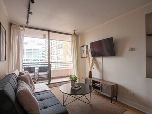 Ein modernes Wohnzimmer mit einer Couch, einem Couchtisch, einem Flachbildfernseher und einem Balkon mit Blick auf Gebäude.