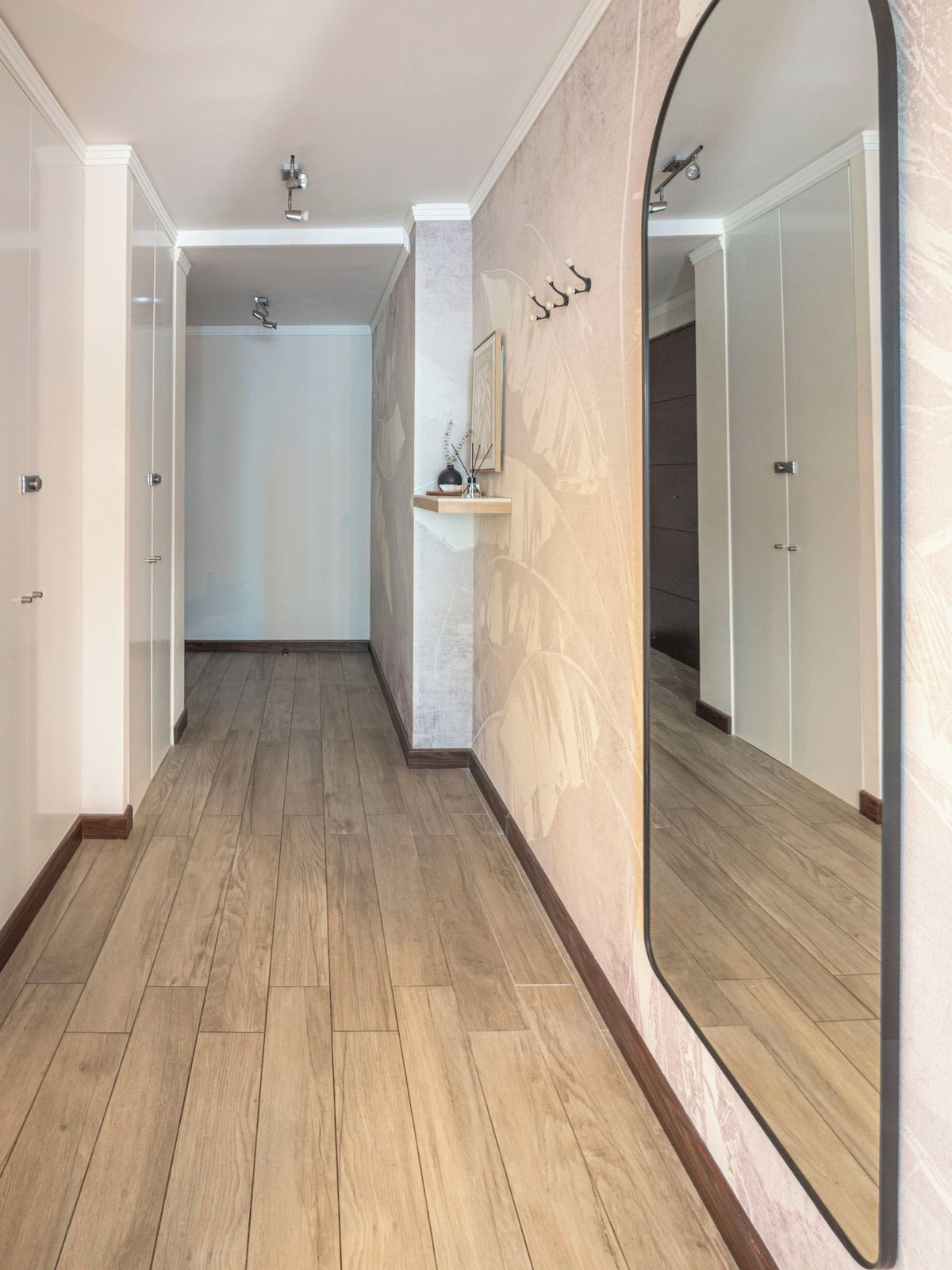 Ein Flur mit Holzboden, einem großen Spiegel und einem an der Wand befestigten Regal mit einer Vase.