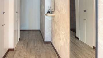 Un pasillo con piso de madera, un espejo grande y un estante de pared con un florero.
