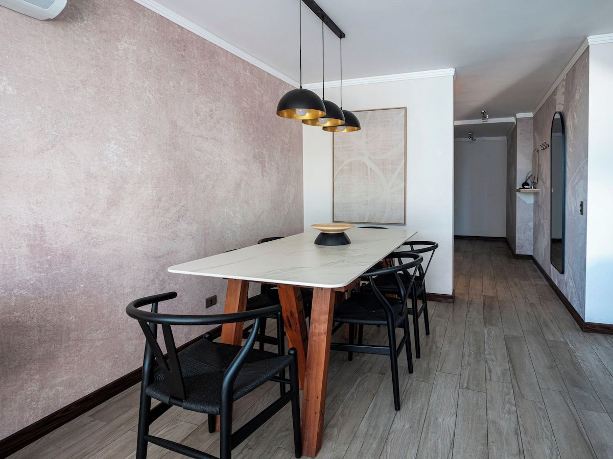 Un espace repas avec une table blanche, des chaises noires et un luminaire suspendu noir.