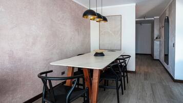 Un espace repas avec une table blanche, des chaises noires et un luminaire suspendu noir.