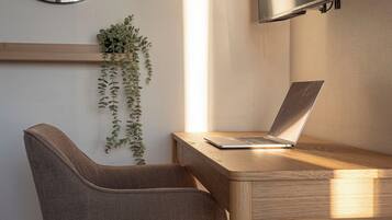 Un espacio de trabajo moderno con una computadora portátil sobre un escritorio de madera, una silla, una planta colgante y un televisor montado en la pared.