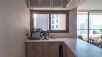 Une cuisine moderne avec des meubles en bois, une machine à café et une fenêtre donnant sur un paysage urbain.