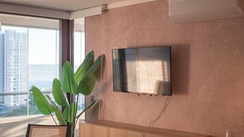 Moderni hotellihuone, jossa on suuri ikkuna, seinälle asennettu taulutelevisio, puinen työpöytä ja ruukkukasvi.
