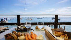 A table with seafood, wine glasses, and bread, overlooking a marina with boats. - Holiday Home 'Villa L'escale 600 M De La Plage' with Private Terrace and Private Garden (Andernos-les-Bains)