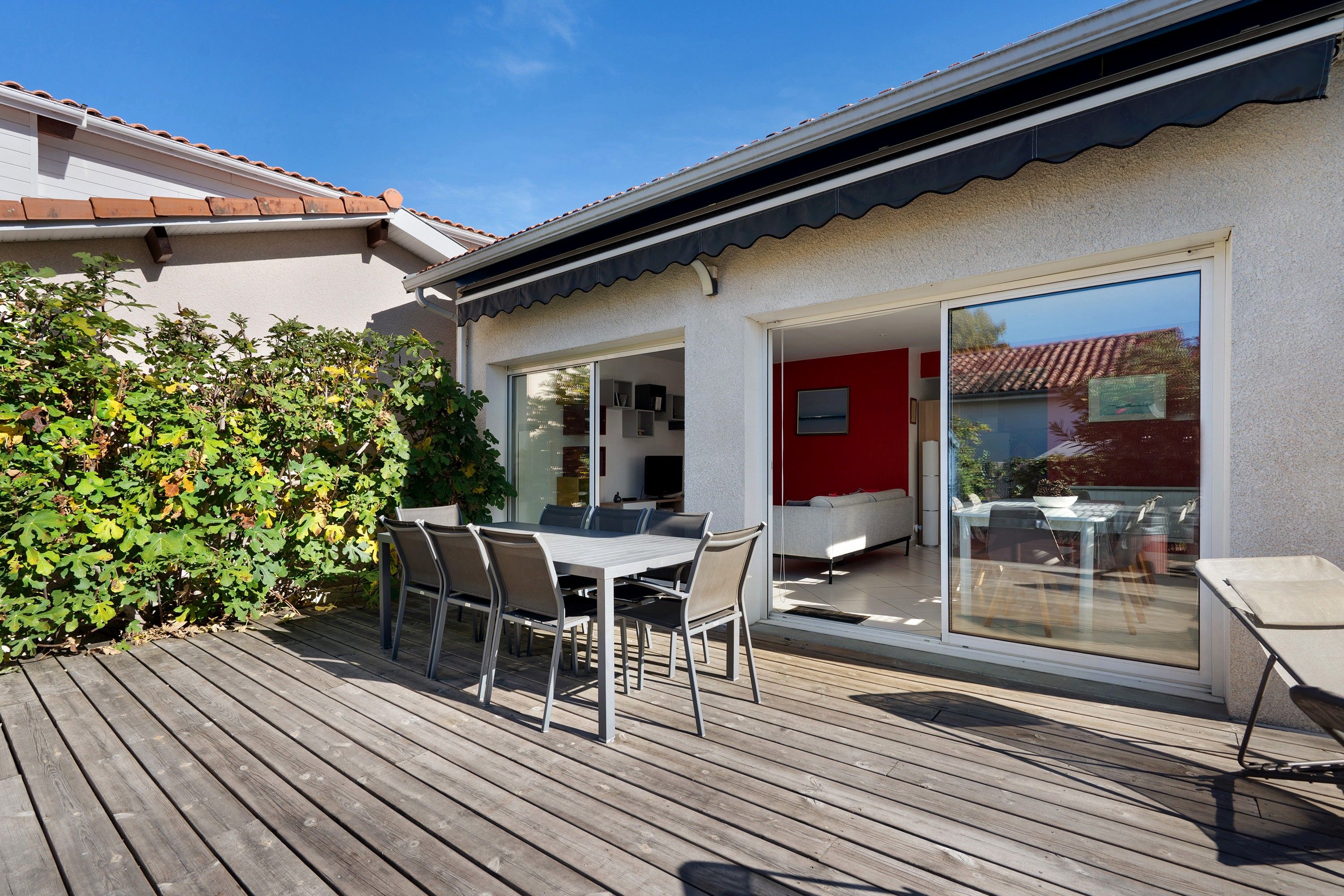 Eine Terrasse mit Tisch und Stühlen, eine rote Wand und eine Glastür zu einem Innenraum.
