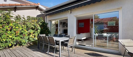 En terrasse med et bord og stole, en rød væg og en glasdør, der fører ind i et rum.