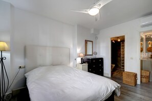 Een slaapkamer met een groot bed, nachtkastje, lamp, kapstok en een spiegel aan de muur.