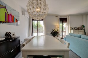Un comedor moderno con una mesa y sillas blancas, una lámpara decorativa en el techo y vistas amplias por grandes ventanales.