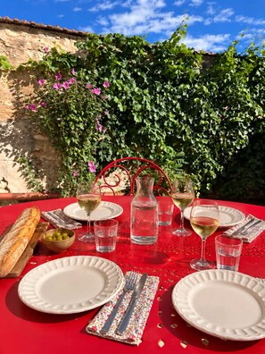 An outdoor dining setup with a red table, white plates, and glasses of wine, set against a backdrop of greenery and a stone wall. - Charming 2-bedroom house with AC in center of Chablis (Chablis)