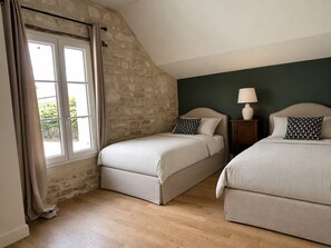 A bedroom with two beds, a window with curtains, a lamp on a bedside table, and a stone wall. - Charming 2-bedroom house with AC in center of Chablis (Chablis)