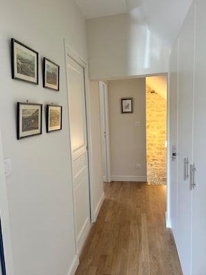 A hallway with wooden flooring, white walls, and framed pictures on the left. - Charming 2-bedroom house with AC in center of Chablis (Chablis)