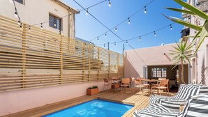 A pool area with a wooden deck, a seating area with striped cushions, and string lights. - Spacious 4-bedroom apartment in peaceful Cape Town with AC (Cape Town)