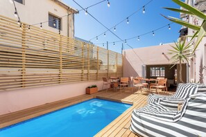 Ein Poolbereich mit Holzterrasse, einer Sitzecke mit gestreiften Kissen und Lichterketten.