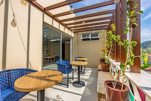 Eine Terrasses mit Holztischen und blauen Stühlen, einem mit Lichterketten geschmückten Pergola und Kübelpflanzen.