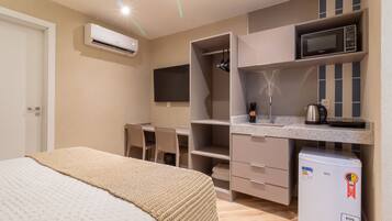 A compact hotel room with a bed, kitchenette, and a TV mounted on the wall.