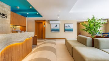 Un área de recepción con mostrador de madera, mostrador de atención al cliente, zona de estar con sofás y una planta.
