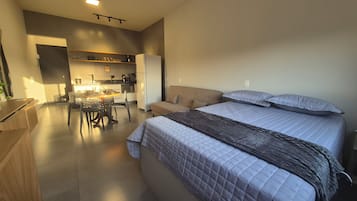 Un dormitorio moderno con una cama grande, un sofá y una zona de cocina al fondo.