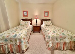 A room with two single beds, a nightstand with a lamp, and two framed pictures on the wall. - Pelican Bay: Views, Pool & More! (Escambia County)