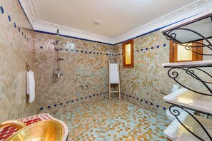 Casa de banho com chão em azulejos, chuveiro, porta-toalhas, sanita e janela.