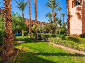 Un jardin bien entretenu, agrémenté de palmiers, d’une pelouse verdoyante et d’un bâtiment à la façade beige.