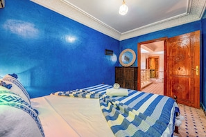 Une chambre avec deux lits, une porte en bois et une vue sur un couloir.