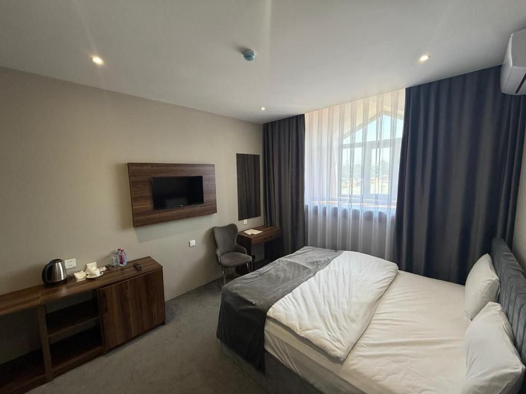 Een hotelkamer met een bed, een bureau, een stoel, een aan de muur bevestigde televisie en een raam met gordijnen.
