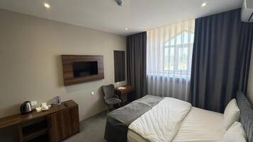 Een hotelkamer met een bed, een bureau, een stoel, een aan de muur bevestigde televisie en een raam met gordijnen.