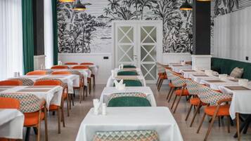 A dining area with tables and chairs, a patterned wall, and a door in the background.