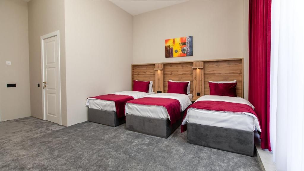Habitación de hotel con tres camas, cabecero de madera, una puerta y una cortina roja.