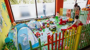 Zona de juegos con diversos juguetes y estructuras recreativas, incluyendo una carpa, una casita y un área de juego cercada.