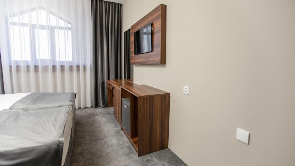 Una habitación de hotel con cama, un escritorio de madera, televisor montado en la pared y una ventana con cortinas.