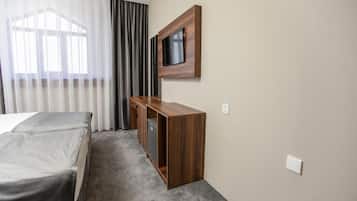 Una habitación de hotel con cama, un escritorio de madera, televisor montado en la pared y una ventana con cortinas.