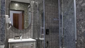A modern bathroom with a glass shower enclosure, a marble-tiled wall, and a built-in sink with a mirror.