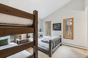 A bedroom with a bunk bed, a single bed, a bedside table, a lamp, and two windows with wooden frames. - Breck Mountain Getaway| Hot Tub+Fireplace+Decks (Breckenridge)