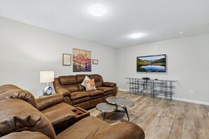 Un salon moderne avec un canapé en cuir marron, une petite table ronde et un téléviseur à écran plat fixé au mur.