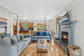 Un salon moderne avec une cheminée, un ensemble de canapés, une table basse et une cuisine en arrière-plan.