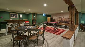 A room with a pool table, chairs, a bar area, and a large wall mural.