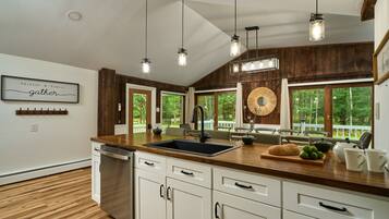 A kitchen with a wooden countertop, white cabinets, and a large window with a view of trees.