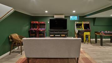 A room with a flat-screen TV, two arcade games, a sofa, and a foosball table.