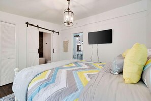 A bedroom with a bed, a TV mounted on the wall, and a door leading to another room.