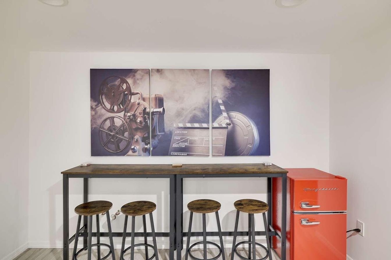 A bar area with a vintage film projector, a red refrigerator, and three stools.
