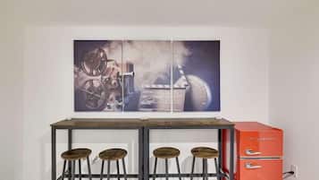 A bar area with a vintage film projector, a red refrigerator, and three stools.