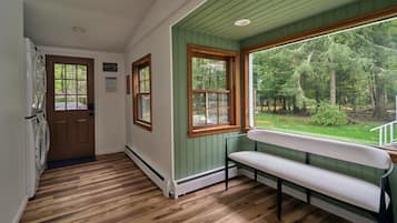 A room with a bench, wooden flooring, a window with a view of a forest, and a door with a sign.