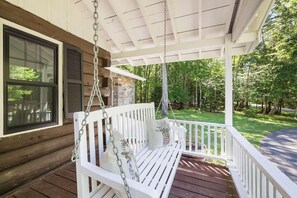 A wooden porch with a white swing bench, a hanging chain, and a stone wall.