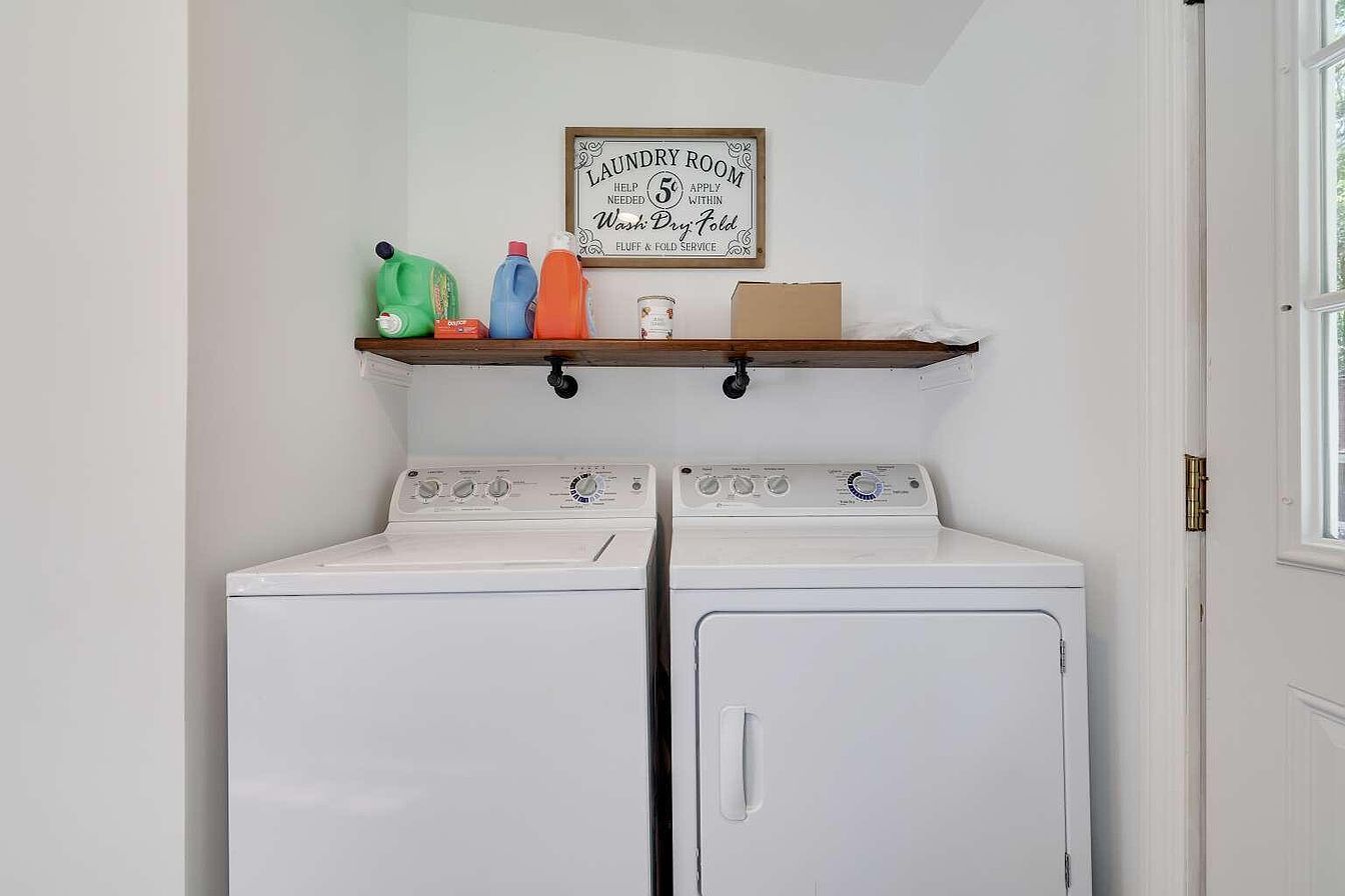 A laundry room with two white washing machines, a shelf with cleaning supplies, and a framed sign above.