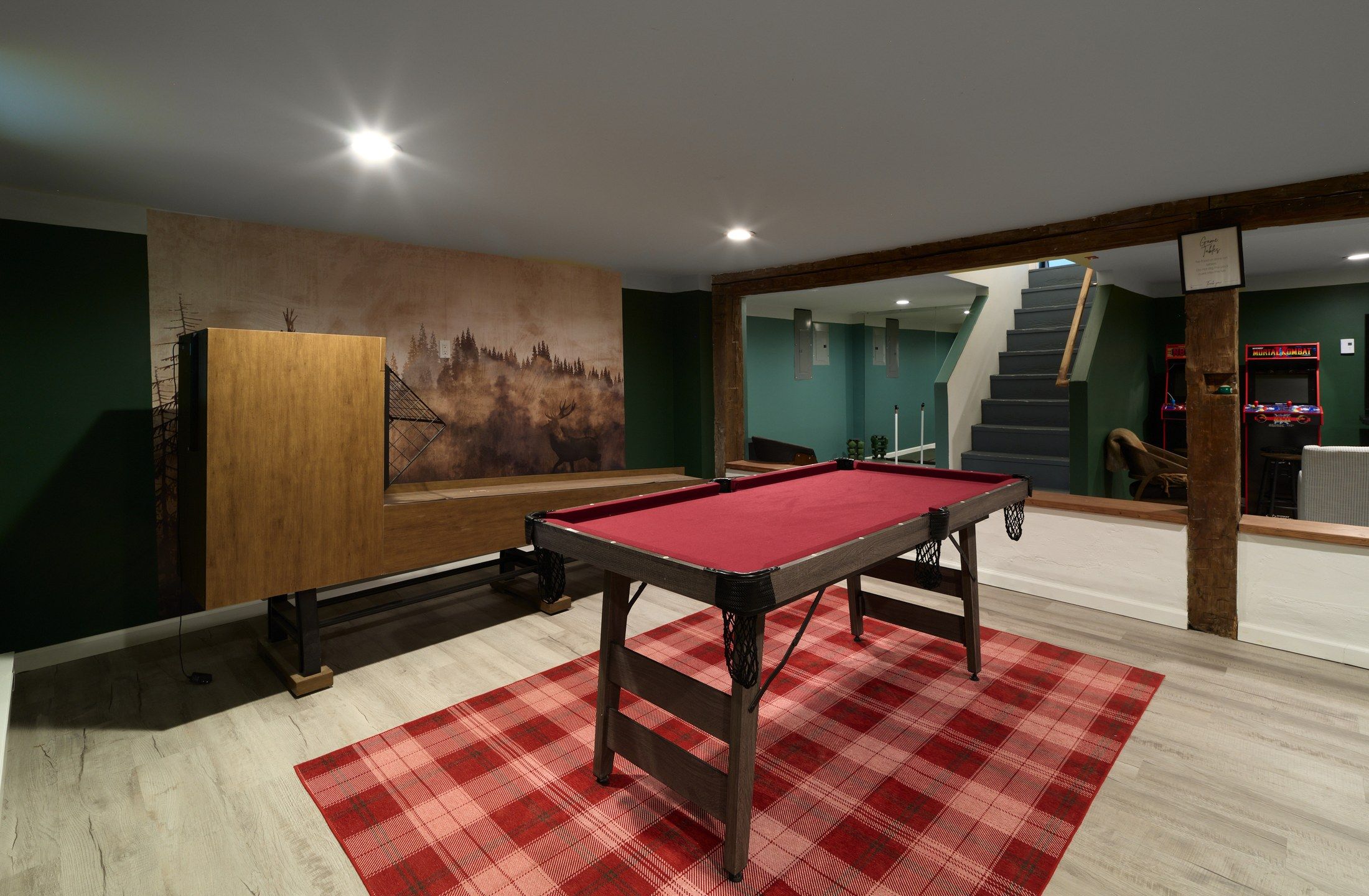 A pool table in a room with a mural, a staircase, and arcade machines.
