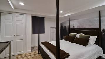 A bedroom with a four-poster bed, a large window with a forest view, and a door with a dark panel.